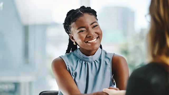 A woman smiling and shaking hands with a colleague
