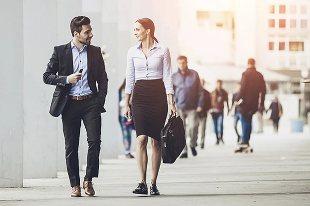 Two people wearing business suits walking and chatting