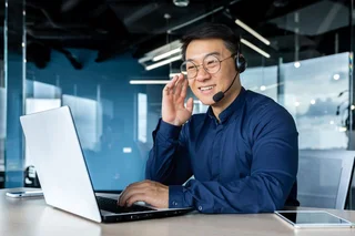 Person wearing a headset working on a laptop in a modern office environment.
