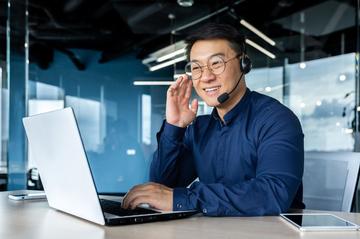 Person wearing a headset working on a laptop in a modern office environment.
