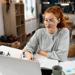 Woman with red hair smiling looking at a computer laptop
