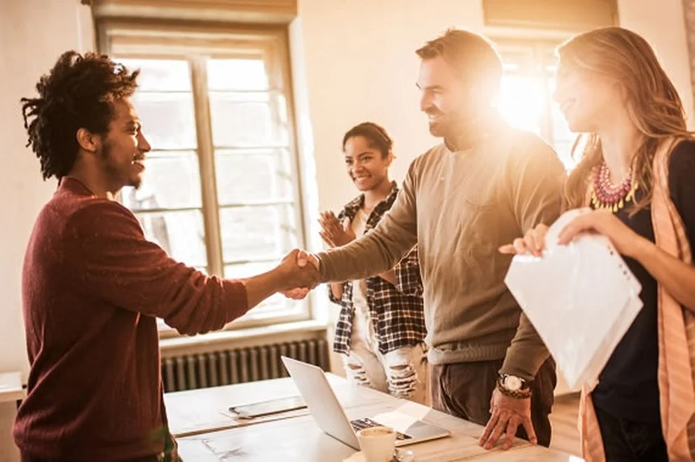 People standing over a table with laptops and documents and shaking hands
