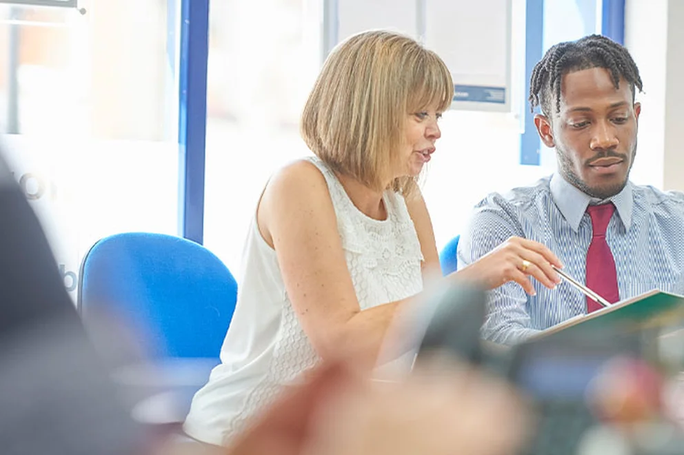 A woman goes through work on a tablet with her employee while they're at a desk.