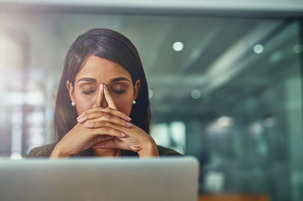 Woman sitting at a desk in front of a laptop with eyes closed and hands ina concentrated position
