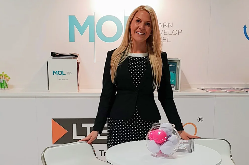 Woman wearing a business suit and standing in front of a wall with MOL Learn logo