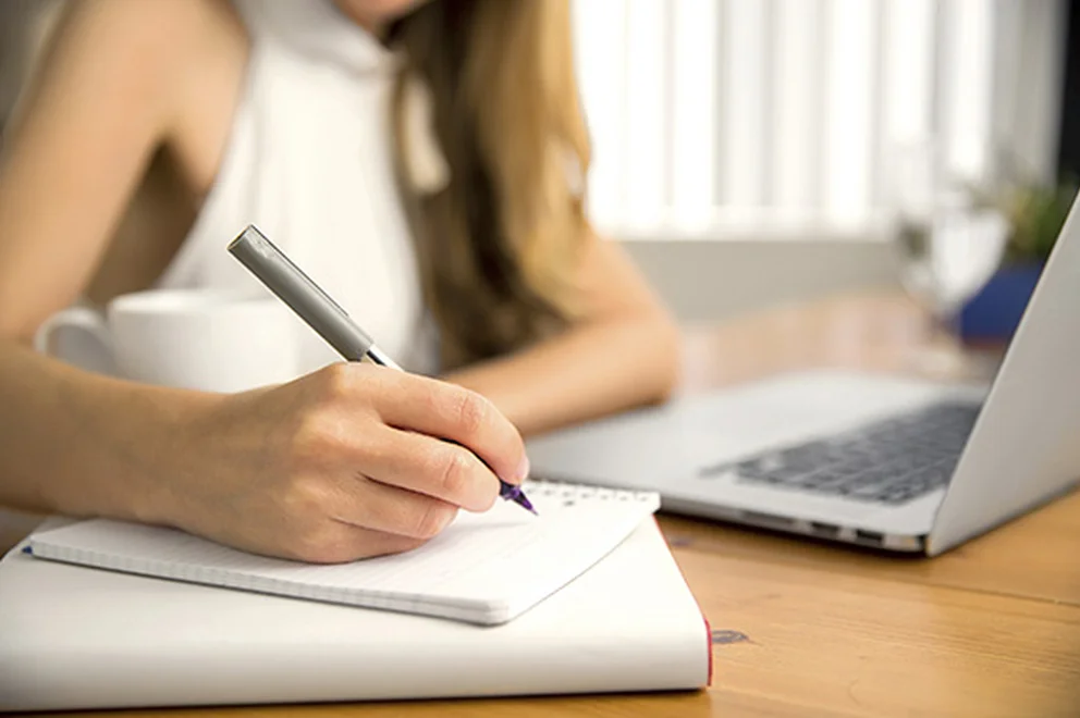 Close up of a woman's hand holding a pen and working on a laptop
