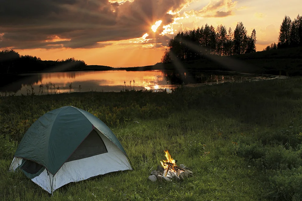 A tent and a campfire by a lake at sunset