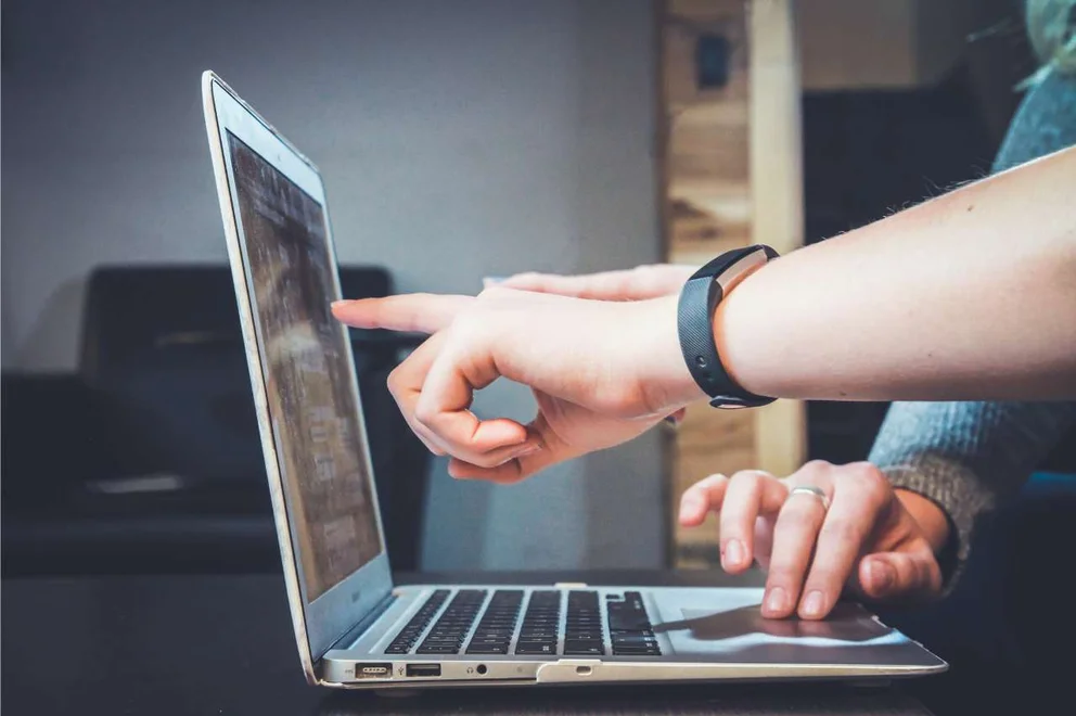 Human hands pointing at a laptop computer screen