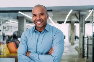 Person in a light blue shirt standing with arms crossed in a modern office workspace.