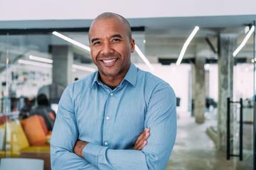 Person in a light blue shirt standing with arms crossed in a modern office workspace.