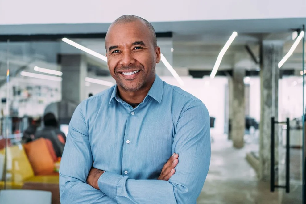 Person in a light blue shirt standing with arms crossed in a modern office workspace.