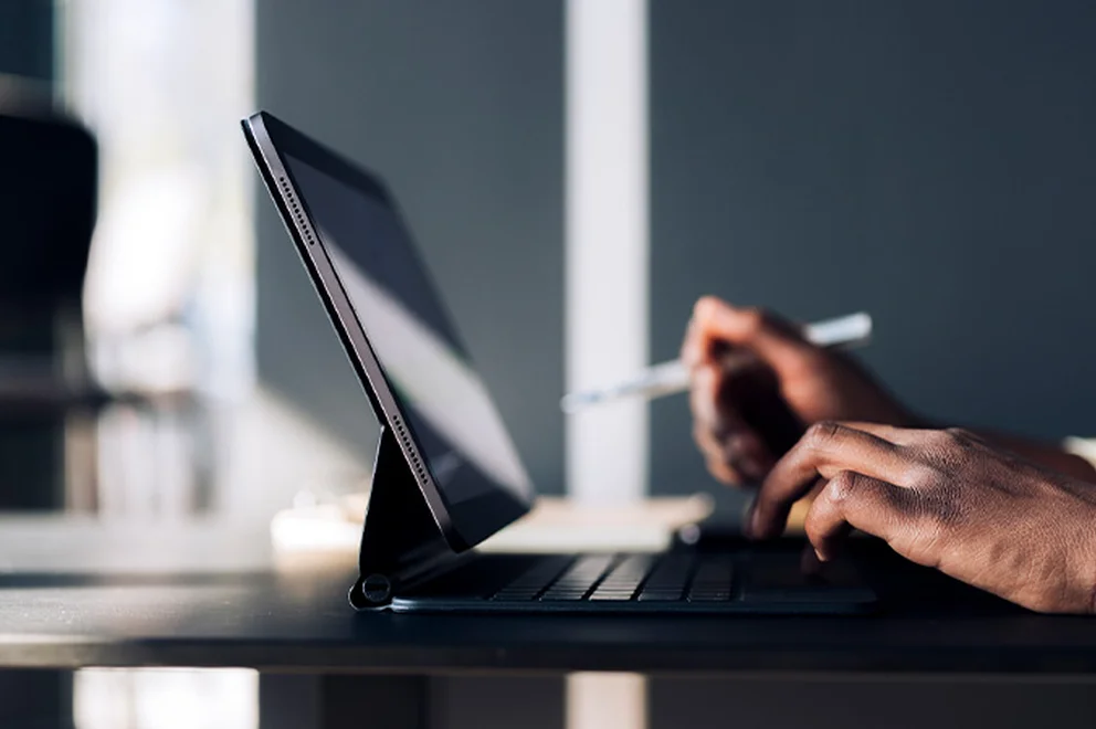It's a side view of a tablet and laptop, with one hand poised over the keyboard and the other holding a pen.