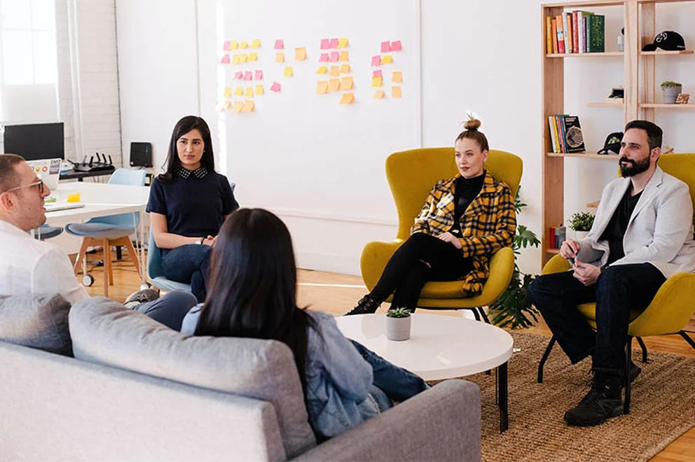 Five people sitting on chairs and on an opposite sofa looking at each other and chatting