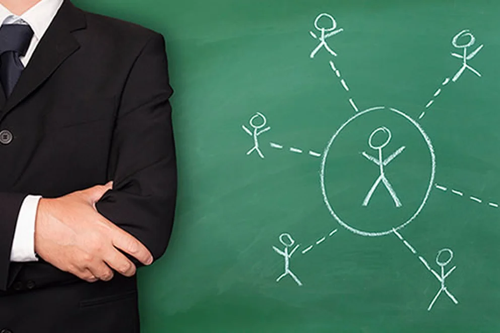 Close up of a man wearing a suit next to a green blackboard with white chalk drawings of stick figures