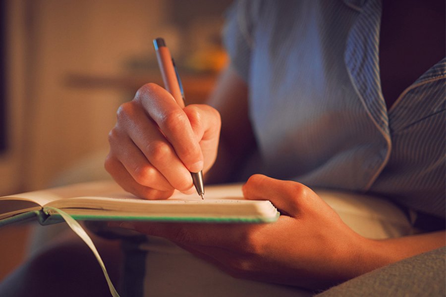 A woman is writing in a notepad with a pen.