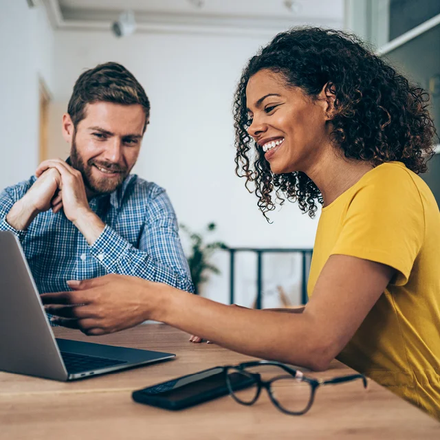 two smiling people working on a laptop computer