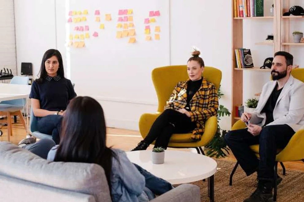 A group of young people sitting in mustard armchairs and on a sofa while chatting