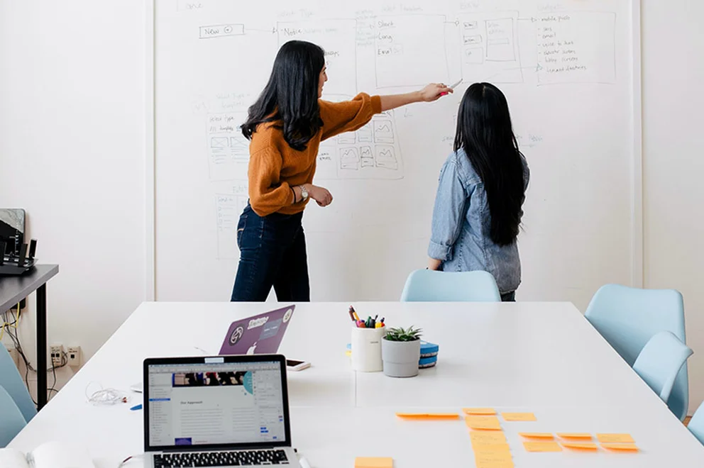 Two women in an office discuss plans.