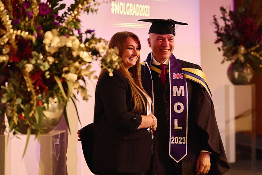 Khaled Shaker is shaking hands with Melanie Nicholson, Managing Director of MOL, at the MOL graduation ceremony. They are on stage.