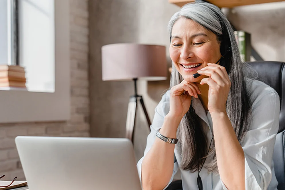 A woman is wearing a headset and speaking on a team call on her laptop.
