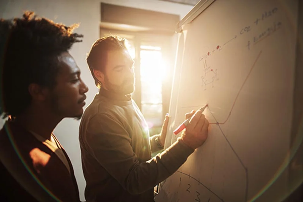 Two people standing in front of a whiteboard and drawing charts