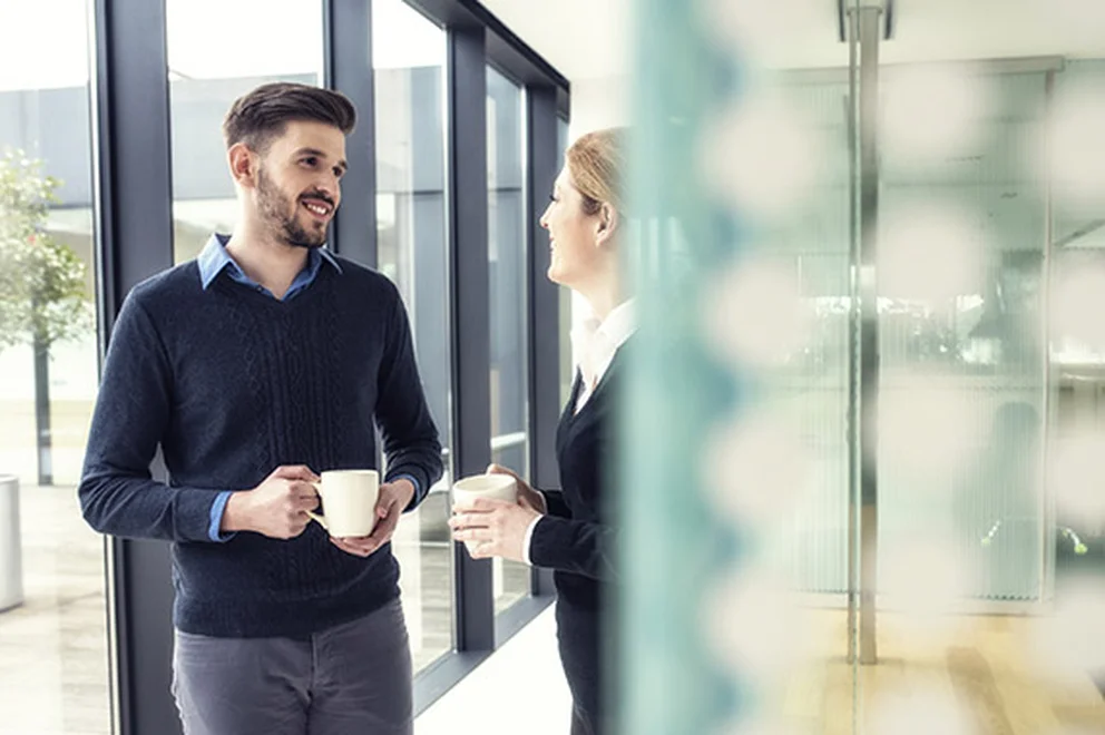 Two people standing and chatting with mugs in their hand
