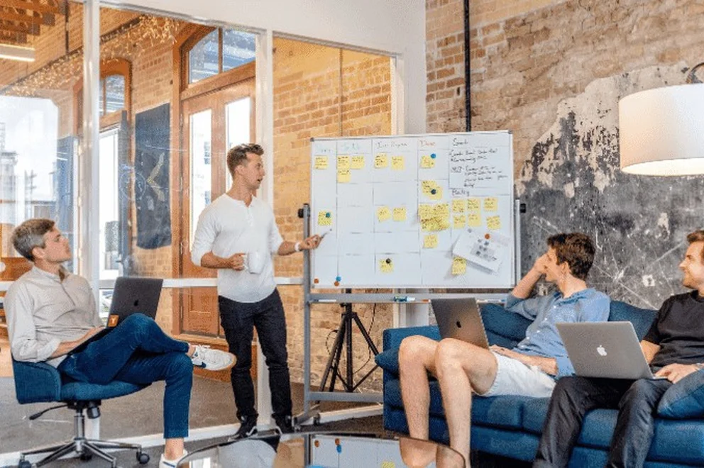 Young person giving a presentation in an office with a whiteboard with many post-it notes