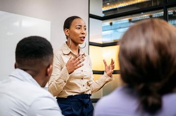Professional giving a presentation to colleagues in a modern office meeting room, leading a business discussion.