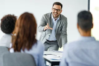 A man is laughing with colleagues in an office setting while he gives a presentation.