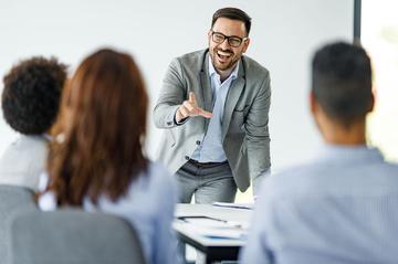 A man is laughing with colleagues in an office setting while he gives a presentation.