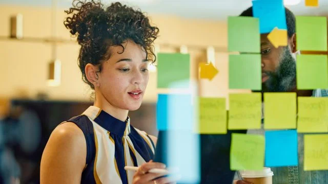 A woman putting up posted notes on a clear board