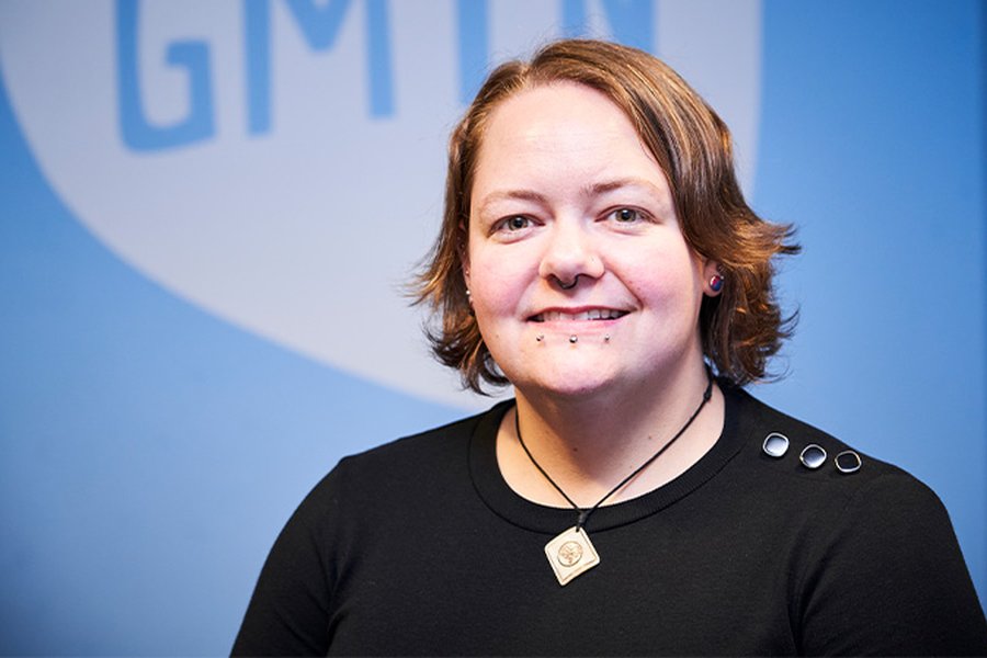 A headshot of Myrtle Finley, Training and Development Manager at the Greater Manchester Youth Network, in front of a light blue wall with the GMYN logo on it.