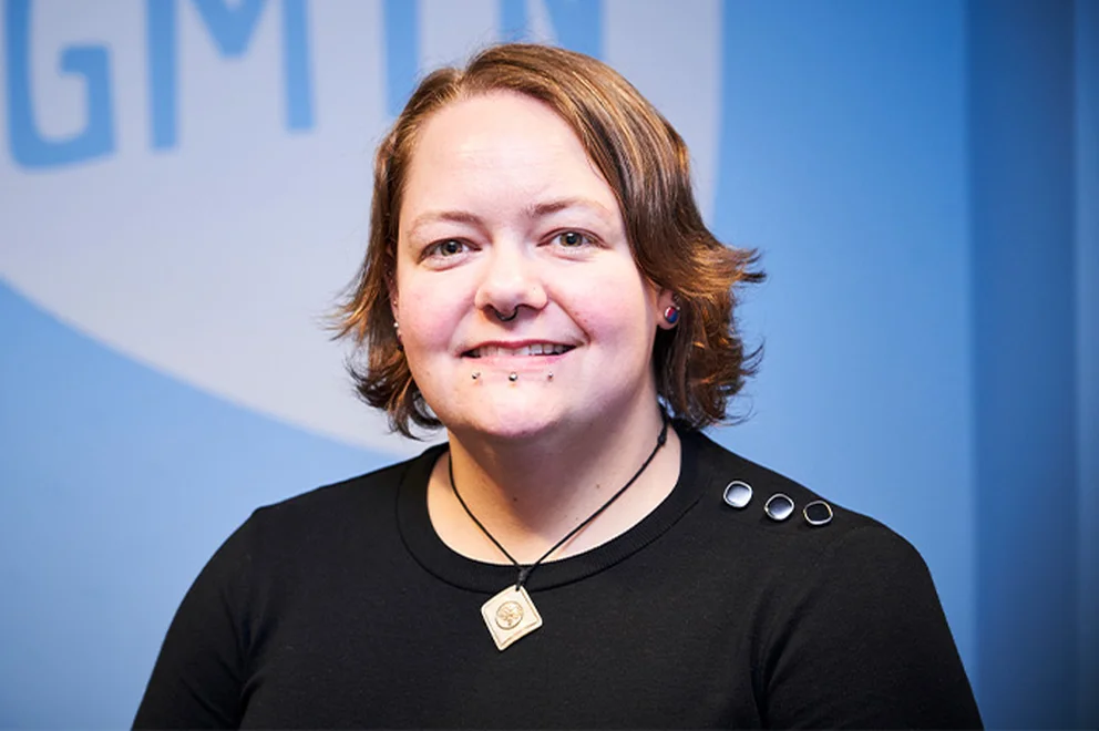 A headshot of Myrtle Finley, Training and Development Manager at the Greater Manchester Youth Network, in front of a light blue wall with the GMYN logo on it.