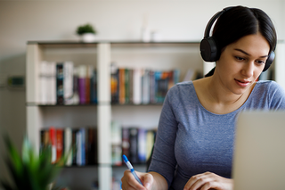 A woman is sat working at her laptop with headphones on.