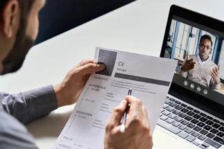 Person reviewing a CV while taking part in a video interview on a laptop.