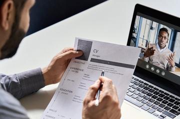 Person reviewing a CV while taking part in a video interview on a laptop.