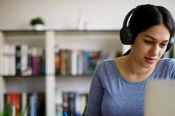 A woman is sat working at her laptop with headphones on.