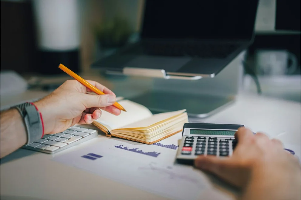 A man doing calculations on a calculator using a pencil and pad.