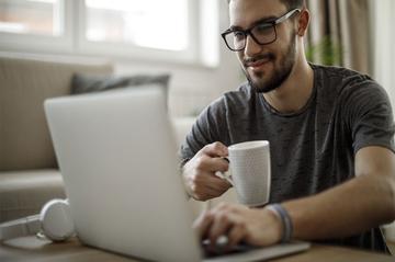 A man sat drinking coffee and typing on a laptop