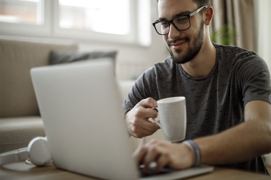 A man sat drinking coffee and typing on a laptop