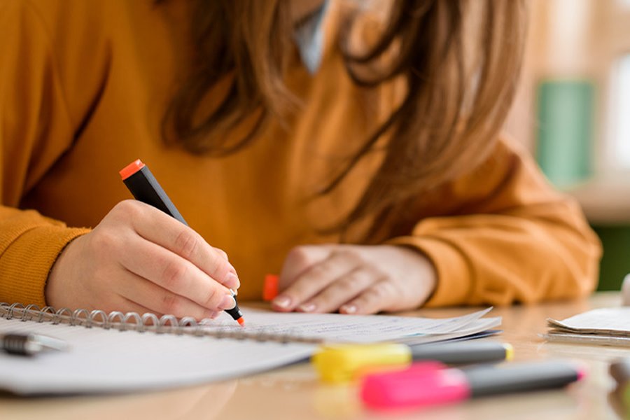 A woman is sat at a desk, highlighting notes on paper.