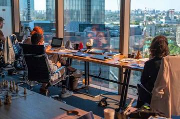 Young people working on laptop computers in front of a big window in an office space