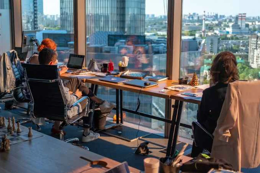 Young people working on laptop computers in front of a big window in an office space