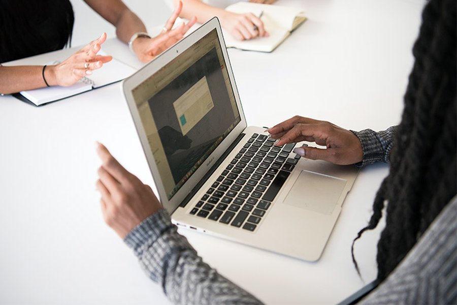 A woman using a laptop and talking to a colleague