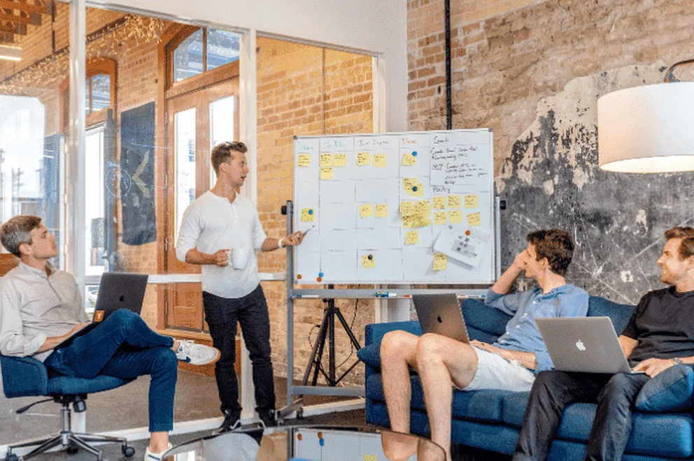 Young person giving a presentation in an office with a whiteboard with many post-it notes