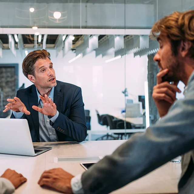 Two men chatting in front of a laptop computer
