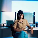 Woman sitting at a desk and facing camera with a computer at her back