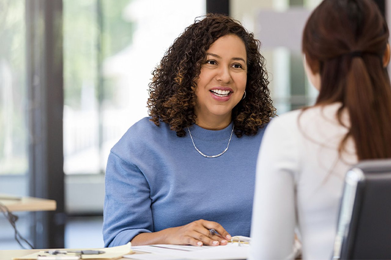 A lady in a blue sweater is hosting a meeting with her employee, who has got their back to the camera.