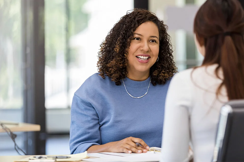 A lady in a blue sweater is hosting a meeting with her employee, who has got their back to the camera.